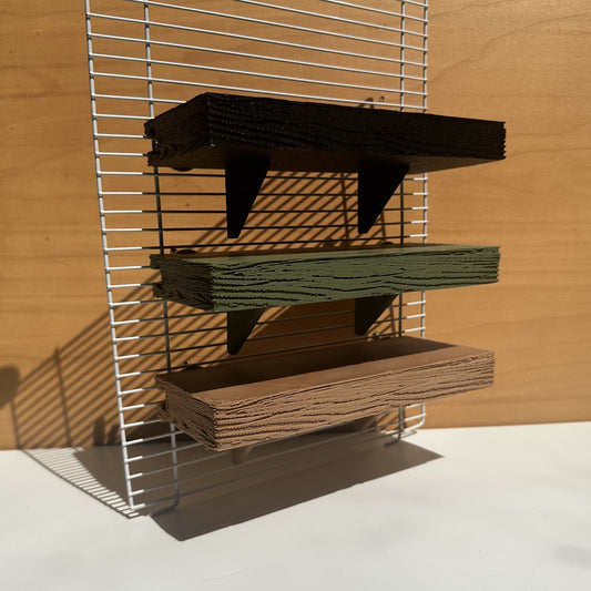 Verstelbare knaagdierplankjes in houtkleur, olijfgroen en zwart – als demonstratie bevestigd aan tralies op verschillende hoogtes.